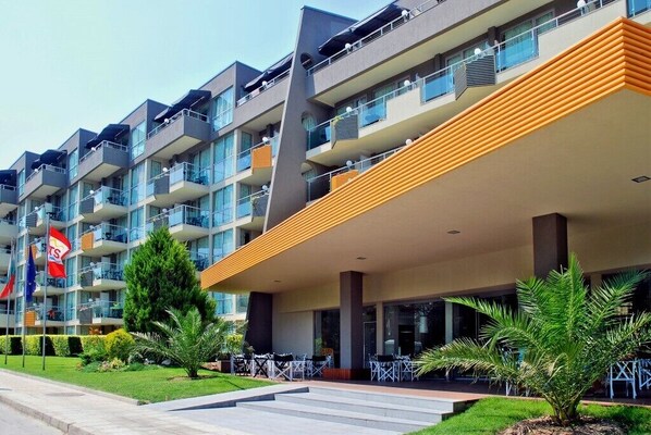 Un hotel de varios pisos con balcones, mobiliario exterior y un jardín cuidado.