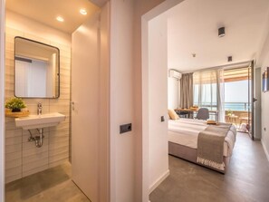 A modern hotel room with a bathroom, a bed, a balcony, and a view of the sea.