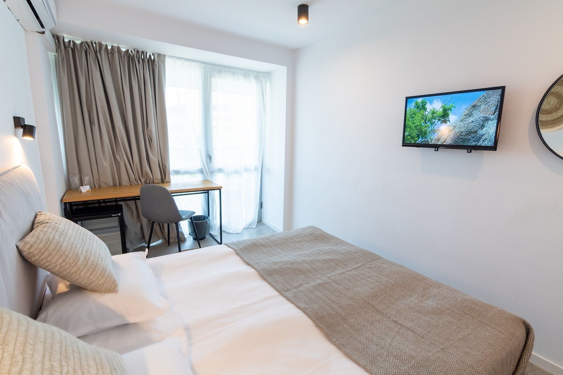 A hotel room with a bed, a desk, a chair, and a TV on the wall.