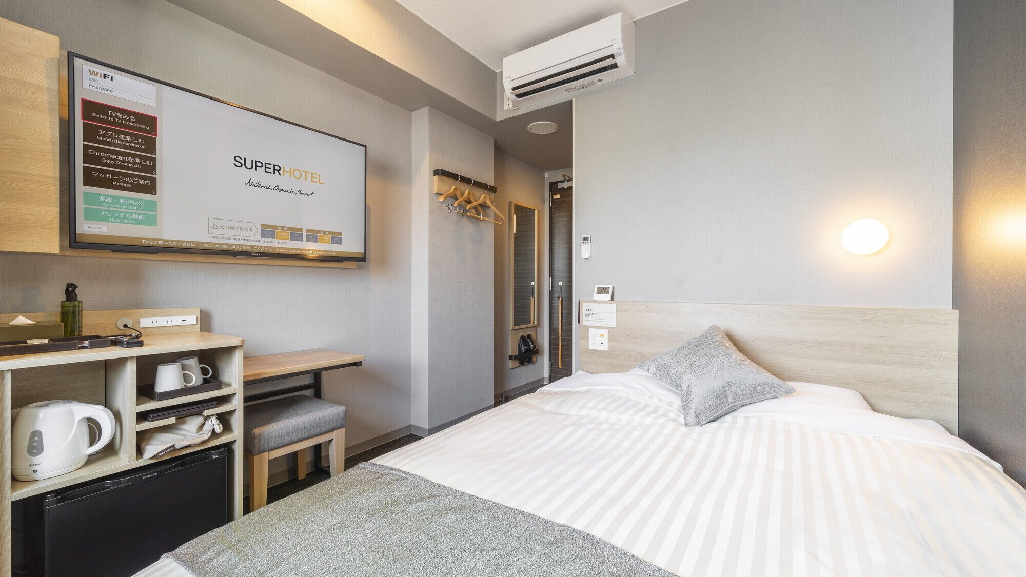 A hotel room with a bed, a desk with a computer, a TV, and a minibar.