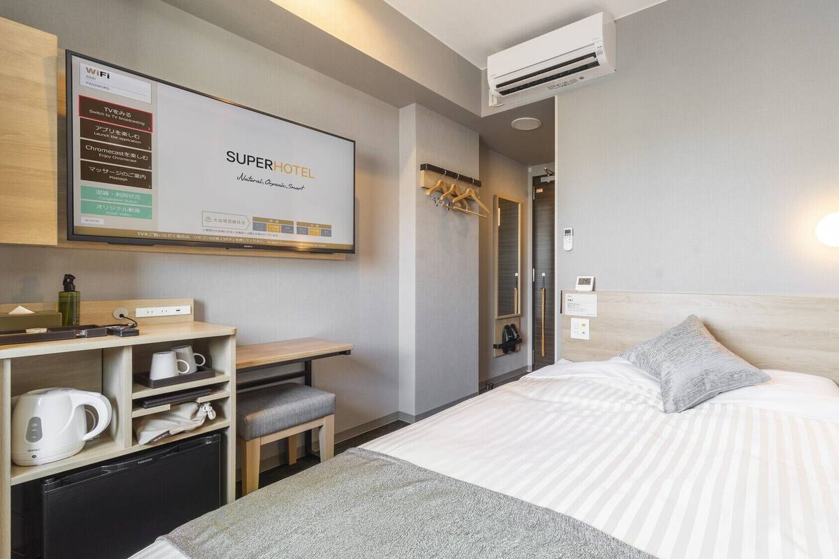 Habitación de hotel con una cama, un escritorio con computadora, televisor y un minibar.