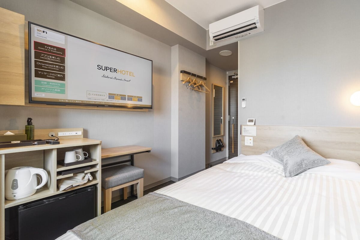 A hotel room with a bed, a desk with a computer, a TV, and a minibar.