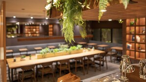 Un comedor moderno con mesas y sillas de madera, una instalación de plantas colgantes y una estantería al fondo.