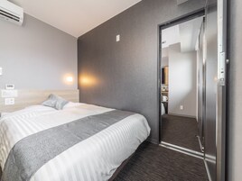 Una habitación de hotel con cama, aire acondicionado de pared, mesita de noche, espejo y puerta que da a un baño.