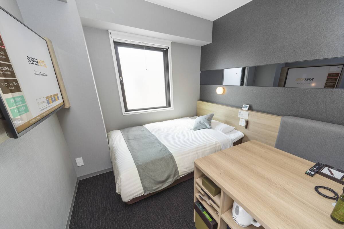 Una habitación de hotel con cama, escritorio, kitchenette pequeño y ventana.