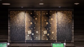 Un área de recepción con un revestimiento de madera oscura y una obra de arte grande y texturizada. Hay dos mostradores de recepción con pantallas digitales.