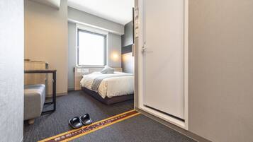 A hotel room with a bed, a desk, a chair, and a window.