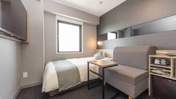 A modern hotel room with a bed, a small desk, a chair, a TV, a window, and a built-in shelf with a coffee maker.