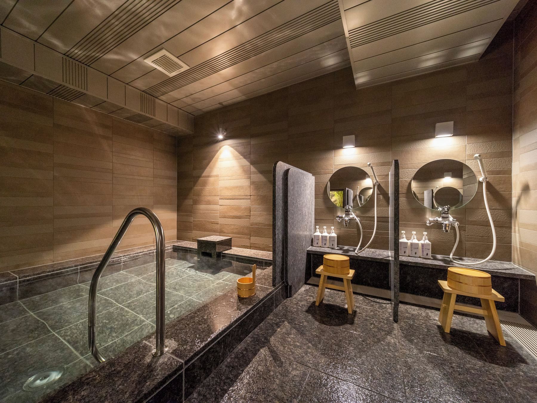 Une salle de bain moderne avec un jacuzzi entouré de parois en verre, des tabourets en bois et une coiffeuse agrémentée de miroirs et d’articles de toilette.