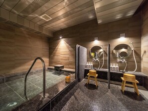 Une salle de bain moderne avec un jacuzzi entouré de parois en verre, des tabourets en bois et une coiffeuse agrémentée de miroirs et d’articles de toilette.
