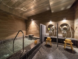 Um banheiro moderno com uma banheira de hidromassagem em vidro, banquetas de madeira e uma pia com espelhos e artigos de higiene pessoal.