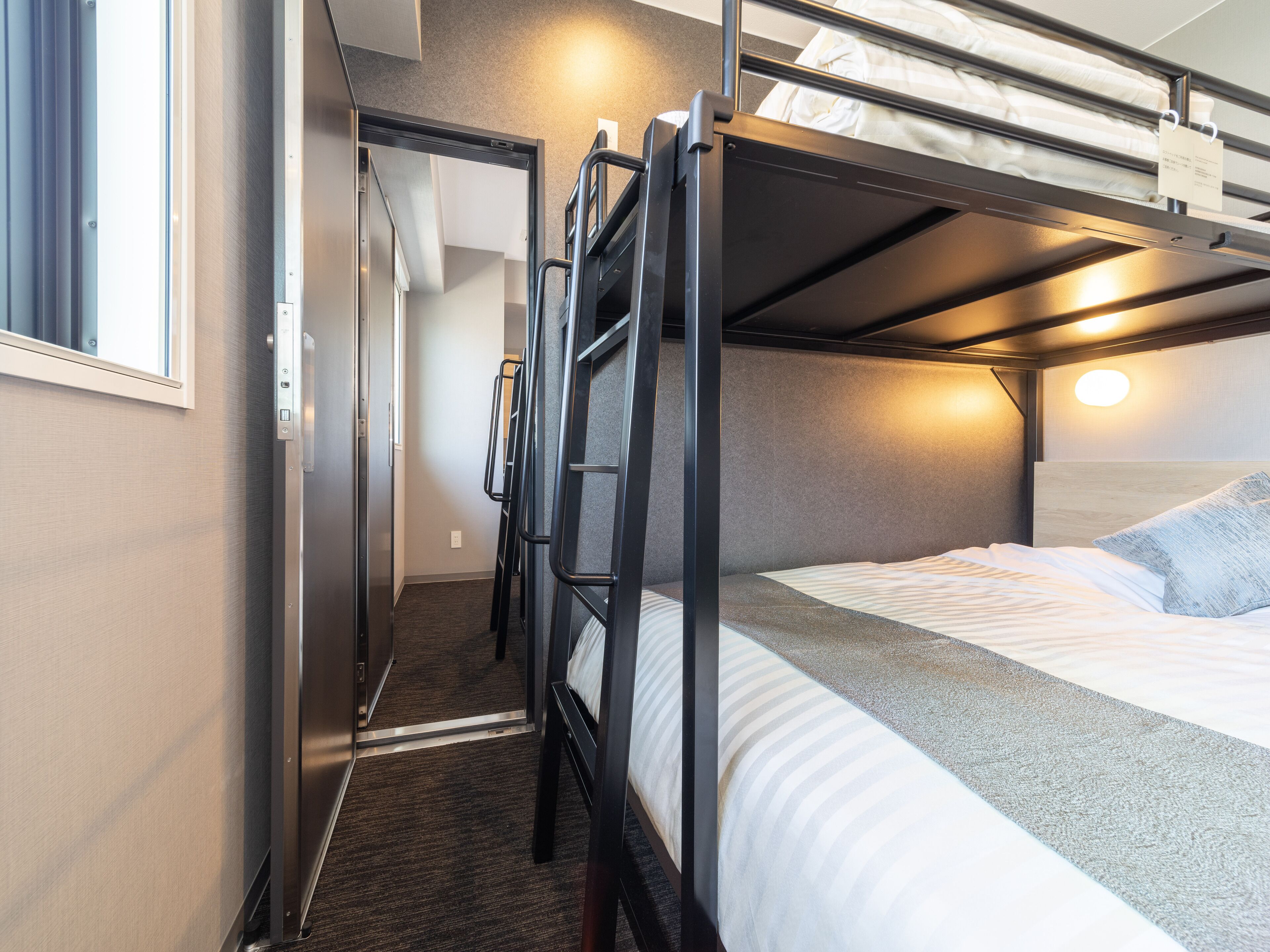 A bunk bed room with a window, a door, and a wall-mounted light fixture.