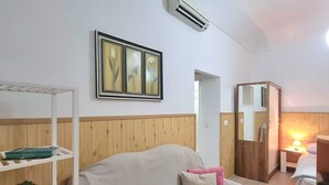 A cozy room with a sofa, a small table with a lamp, a shelf with books and a plant, and a framed picture on the wall. - Heart of the Town (Dubrovnik)