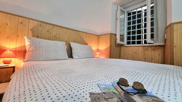 A bedroom with a wooden headboard, two bedside lamps, a window with a view, and a bed with a polka dot bedspread. - Heart of the Town (Dubrovnik)