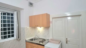 A compact kitchen with a sink, stove, and a small refrigerator. There is a window with a grid pattern and a door with a sign. - Heart of the Town (Dubrovnik)