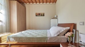 Ein Schlafzimmer mit Bett, Schrank, Nachttisch mit Blumenvase und einem Bild an der Wand.