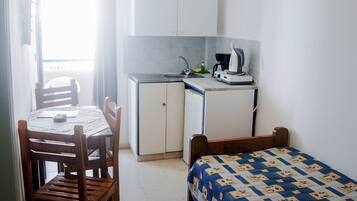 Una habitación pequeña y luminosa con una cama, una mesa con sillas, una kitchenette y una lámpara colgante.