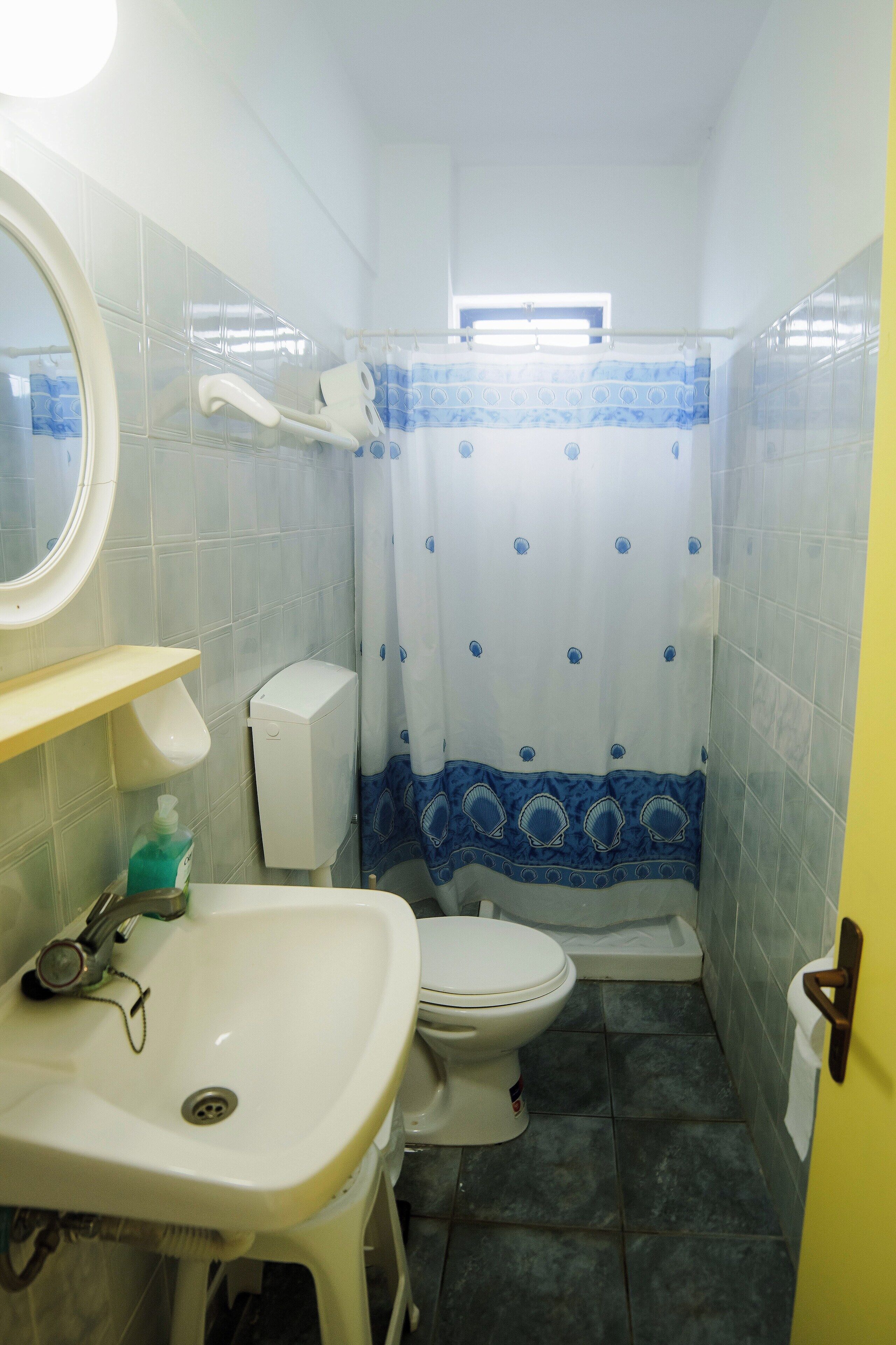 Un baño pequeño con lavamanos, inodoro y cortina de ducha, todo en blanco.