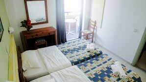 Ein Hotelzimmer mit zwei Betten, einem Holzschrank, einem Spiegel, einem kleinen Tisch mit Blumenvase und Blick auf den Balkon.