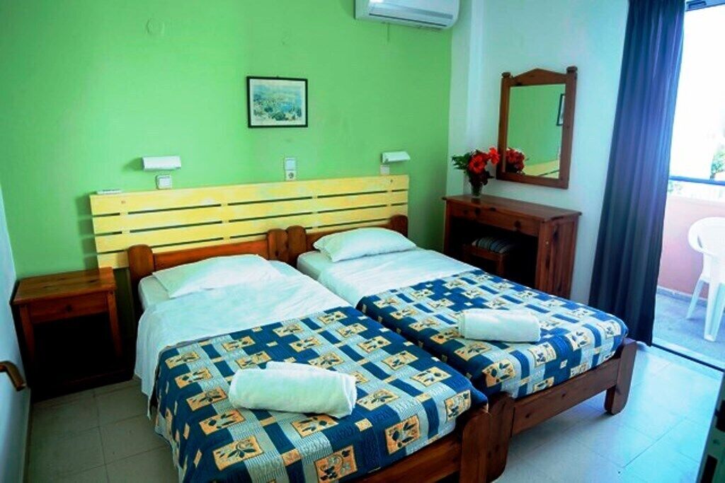 Una cama doble con cabecera de madera, dos mesitas de noche, un espejo y una ventana con cortinas.