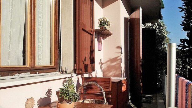 Terrassa exterior amb taula i caires de fusta, una planta penjant i una finestra amb cortines.