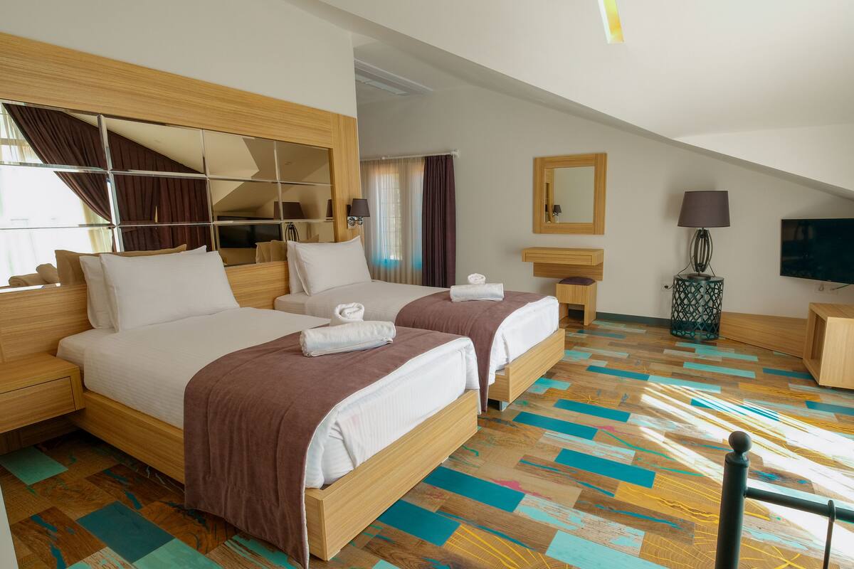 A hotel room with two beds, a TV, a mirror, and a patterned floor.