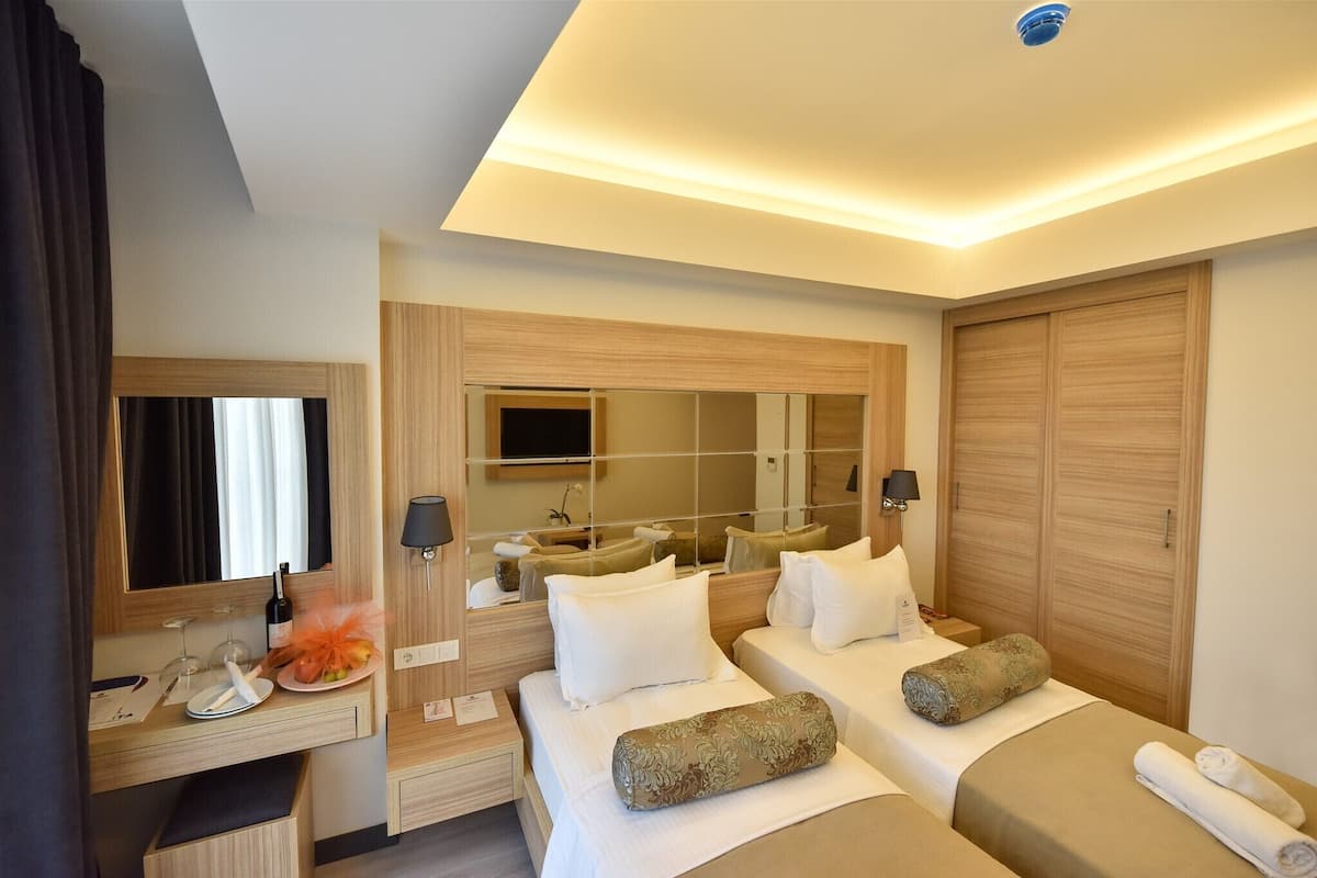A hotel room with a bed, bedside tables, a mirror, a wardrobe, and a desk with a lamp.