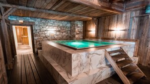 Un espace spa doté d’une piscine en marbre, d’un plancher en bois, de murs en pierre et d’un escalier en bois.