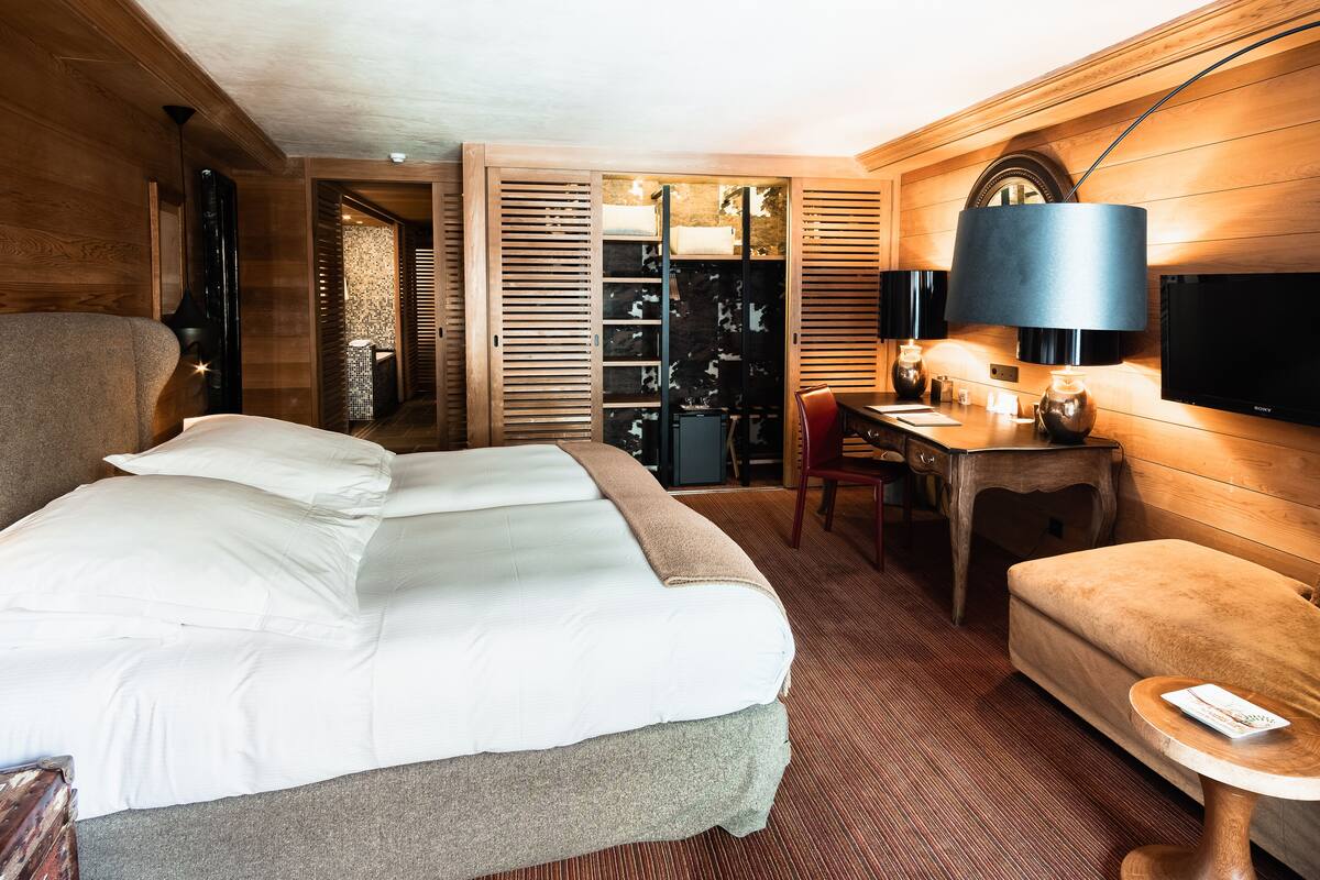 A hotel room with a large bed, a desk, a chair, a TV, and a wardrobe.