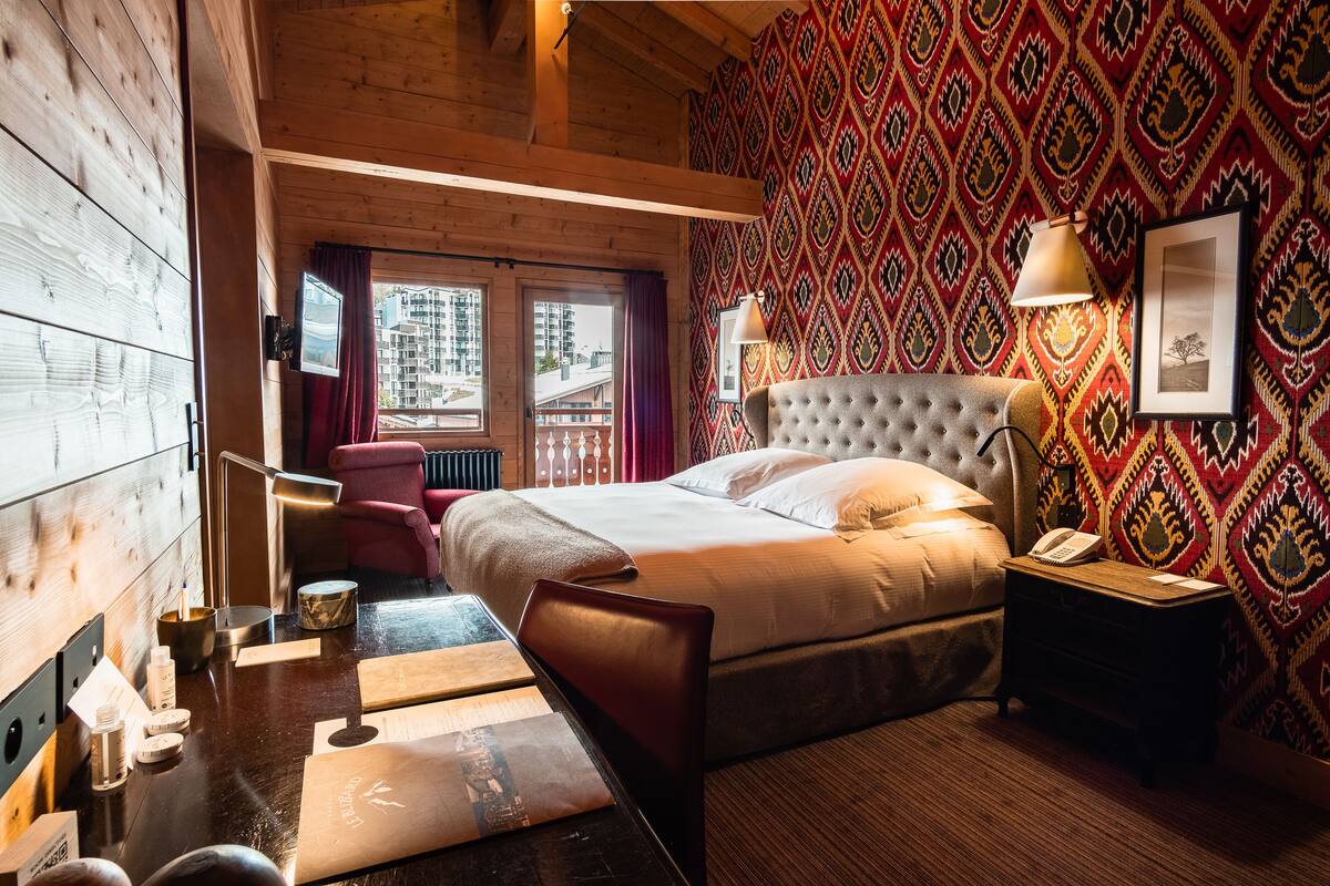 A hotel room with a bed, a desk, a chair, a nightstand, and a window with curtains.