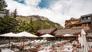 Un espace extérieur aménagé pour les repas, avec des tables, des chaises, des parasols et une piscine.