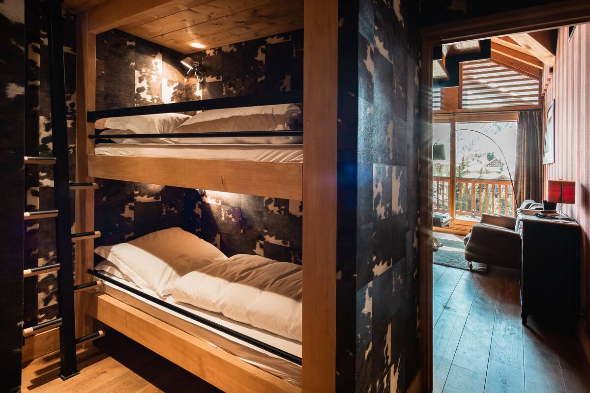 A bunk bed with a wooden headboard, a ladder, and a view of a balcony with a wooden railing.