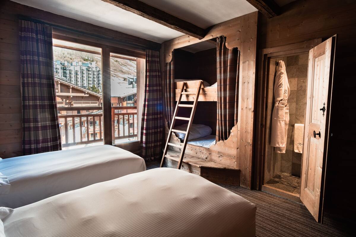 A room with two beds, a wooden ladder, and a bathroom with a wooden door.