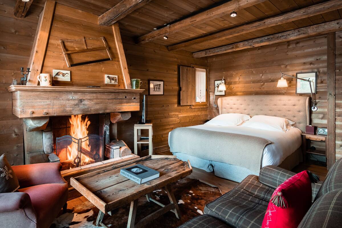A cozy log cabin room with a fireplace, a bed, a small table, and a sofa.