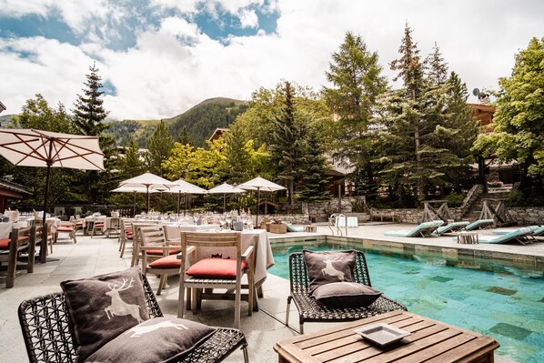 An outdoor pool area with lounge chairs, umbrellas, and dining tables set up for guests.