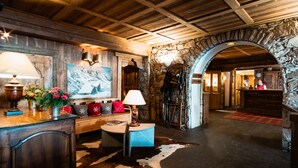 Un hall d’entrée rustique avec des poutres en bois, une arche en pierre, un comptoir d’accueil et un tapis en peau de vache.