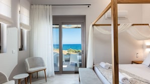 A bedroom with a four-poster bed, a balcony with a view of the sea, and a seating area with chairs and a table. - Lagoon Seaside Villa, Walking distance to the beach & shops!Car Free holiday! (Panormos in Rethymno)