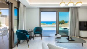 A modern living room with a sofa, two chairs, a coffee table, and a TV. The room has large windows with a view of the ocean. - Lagoon Seaside Villa, Walking distance to the beach & shops!Car Free holiday! (Panormos in Rethymno)