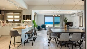 A modern kitchen with a marble countertop, a dining area with a large table and chairs, and a view of the ocean through large windows. - Lagoon Seaside Villa, Walking distance to the beach & shops!Car Free holiday! (Panormos in Rethymno)