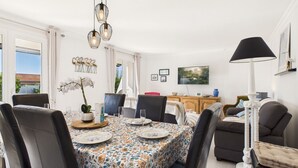 Un comedor con mantel floral, sillas negras, una lámpara de araña y un televisor en la pared.