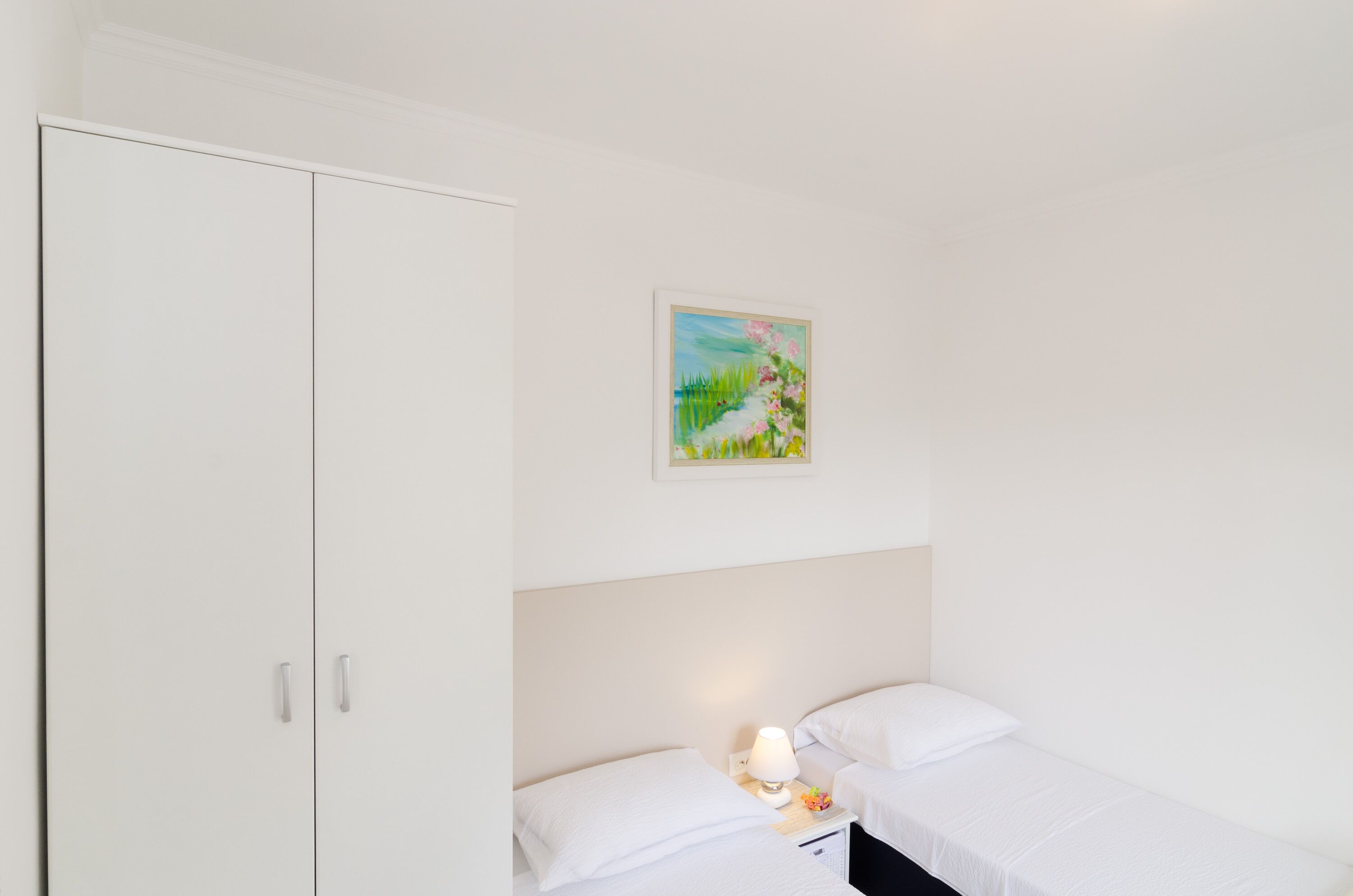 A bedroom with a single bed, a nightstand, a lamp, a wardrobe, and a painting on the wall.