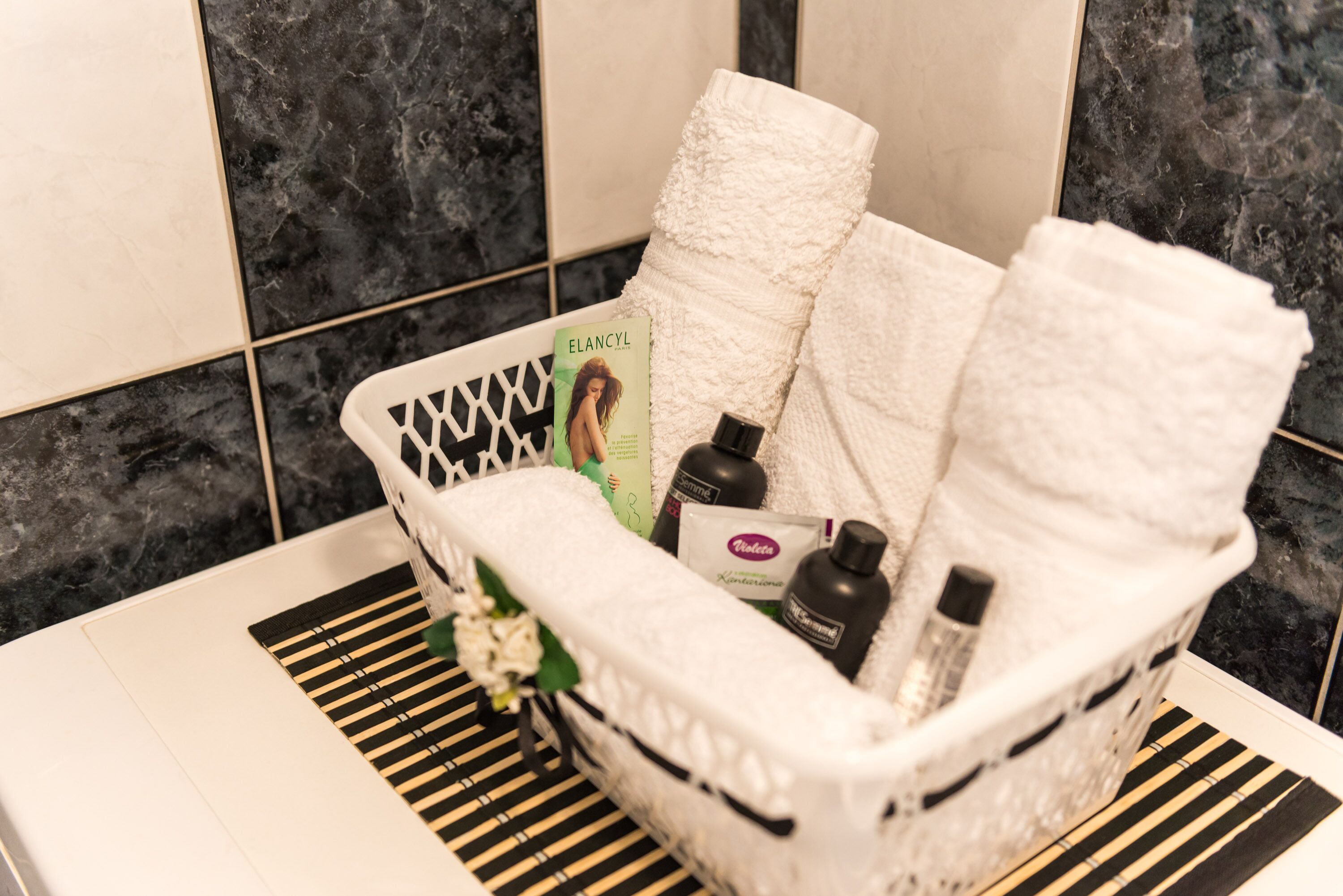 Een badkamer met een wit bad, een zwart-wit gestreept badmatje en een mand met toiletartikelen en een boek.