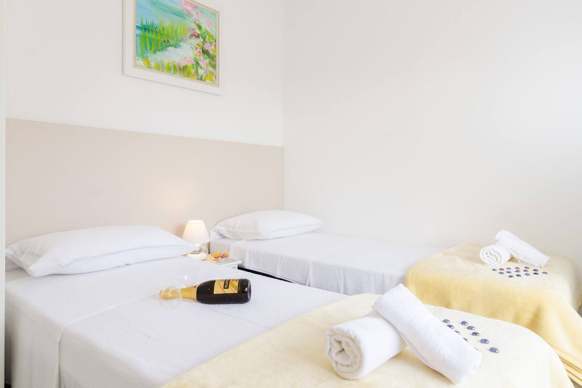 A hotel room with two single beds, a small table with a bottle and a glass, and a towel with decorative buttons.