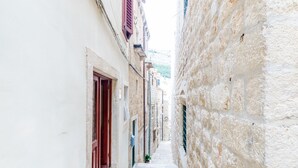 Une ruelle étroite, pavée de pierres, bordée de bâtiments aux volets rouges et aux murs blancs.