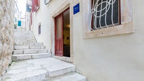 Un escalier étroit en pierre mène à un bâtiment doté d’une porte rouge et d’une enseigne bleue.