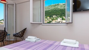 Une chambre d’hôtel avec un lit, deux chaises, une télévision et une vue sur une ville située sur une colline.
