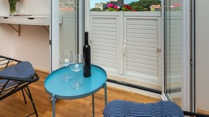 Un balcon donnant sur un paysage urbain, une table avec une bouteille et des verres, et un canapé à rayures.