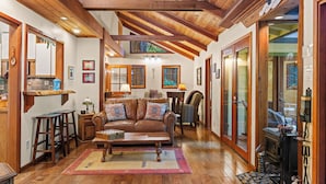 A cozy living room with a wooden ceiling, a fireplace, and a large window.