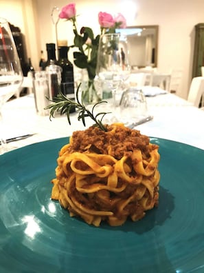A plate of spaghetti with meat sauce, garnished with rosemary, on a teal plate. - Hotel Helvetia (Cervia)