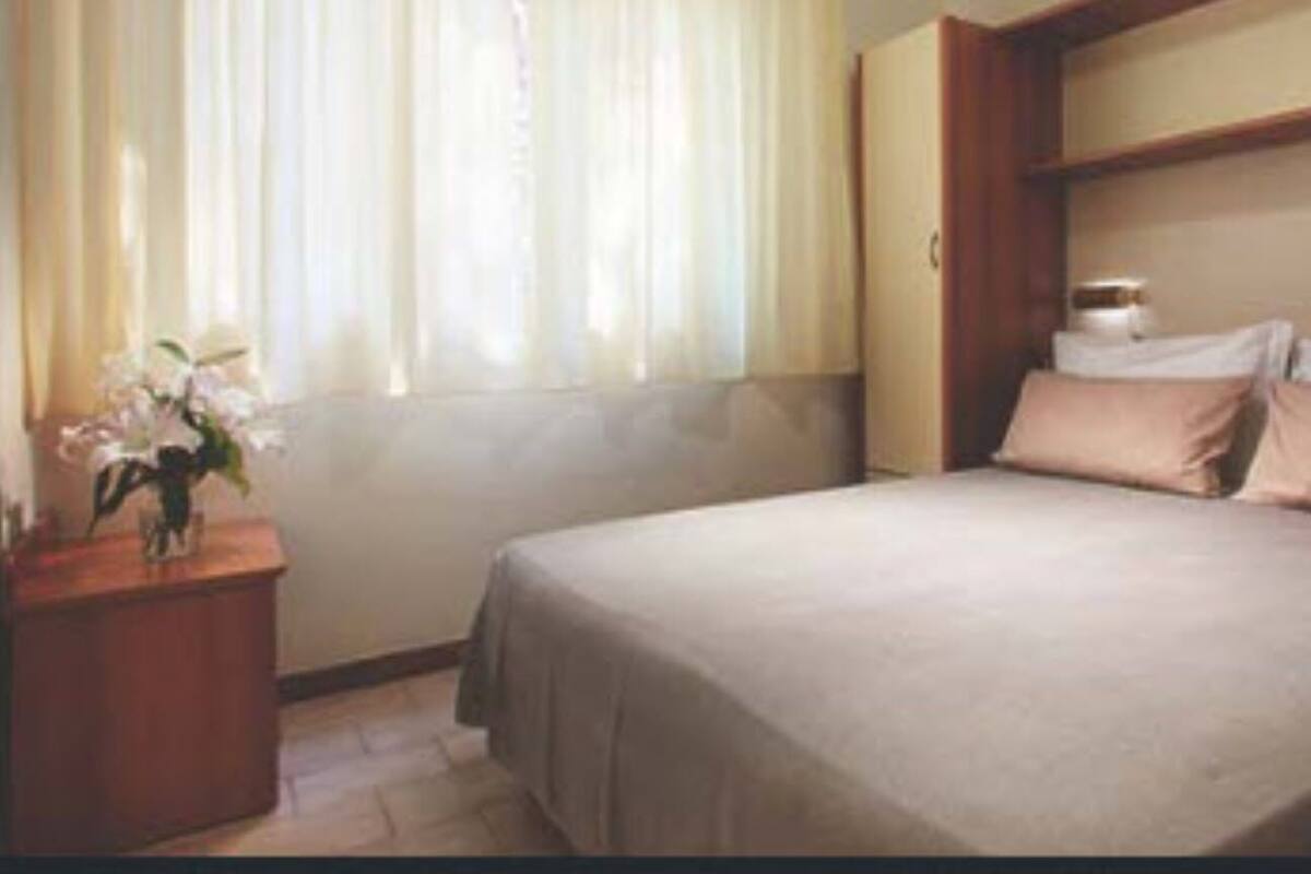 Un dormitorio con cama, mesita de noche y ventana con cortinas.